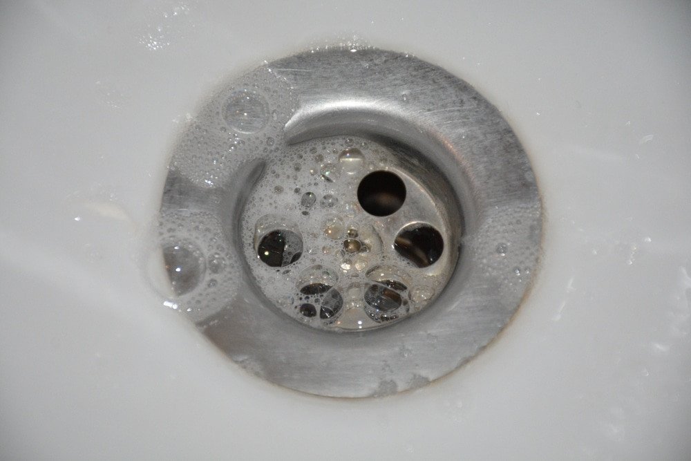 Neglected Drain Blockages. Close-up of a kitchen sink drain with soap bubbles flowing into the stainless steel surface.