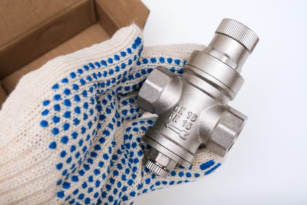 What Causes Poly B Piping to Degrade Over Time in Calgary Properties? pressure-reducing valve. A plumber holding a new water flow regulator, pressure reducer valve in order to replace or mount it, new repair part for plumbing, water supply in a house.