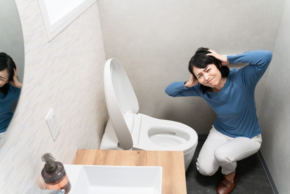 Common Summer Plumbing Problems in Calgary. Toilet Troubles. Lifestyle image of a middle-aged woman suffering from toilet troubles.