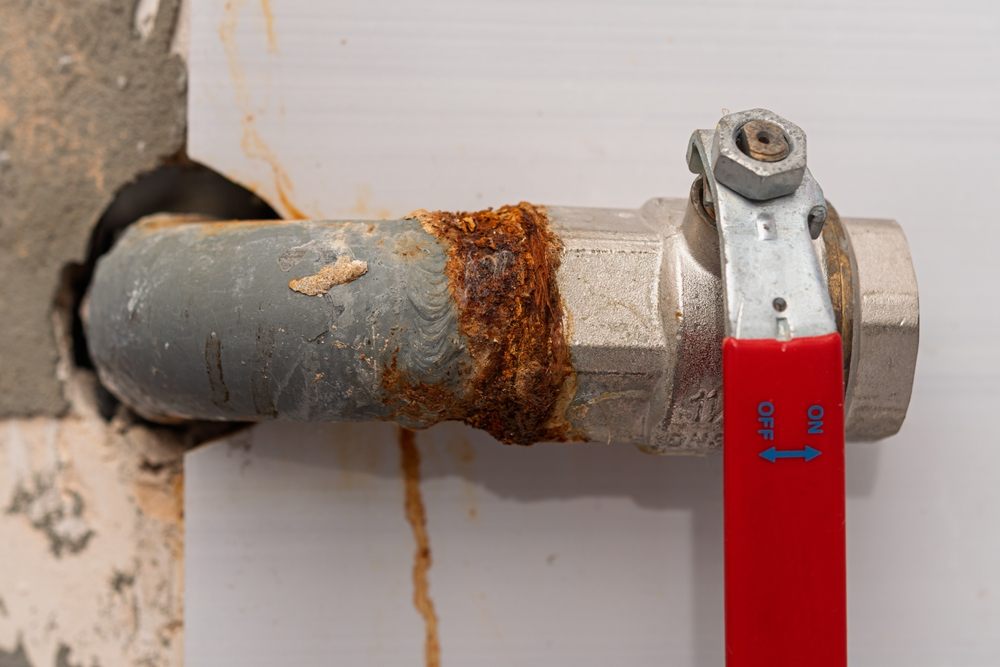 Can Plumbing Services in Calgary Help with Renovation Projects? Rusty metal pipe with ball valve and corrosion stains highlights need for urgent plumbing repair and maintenance in old buildings.