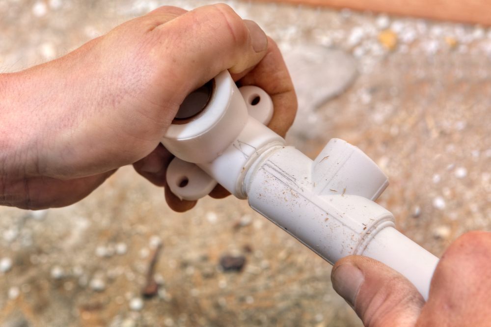 Need Poly B Pipe Repairs? Discover Aquality's Solutions. The plumber connects parts of the Poly B Pipe using fittings in a close-up.