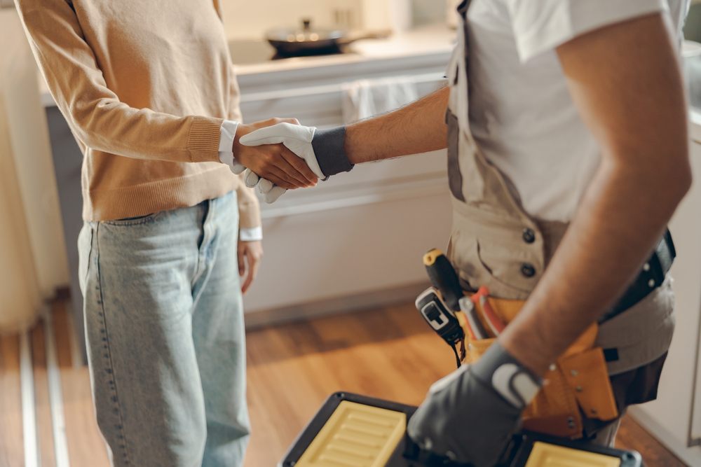 What Makes Aquality Plumbing & Heating the Top Calgary Plumbers? Close up of a plumber in uniform shaking hands with woman while standing at home kitchen.