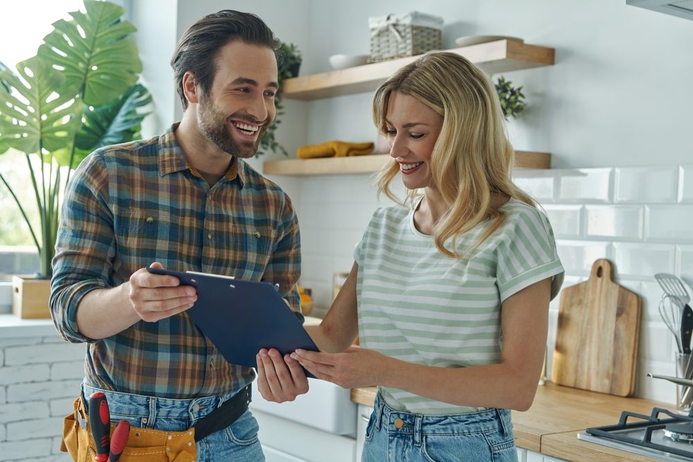 Why Are Aquality’s Calgary Plumbers Experts in Leak Repairs. Beautiful young woman signing document while communicating with plumber in the kitchen.