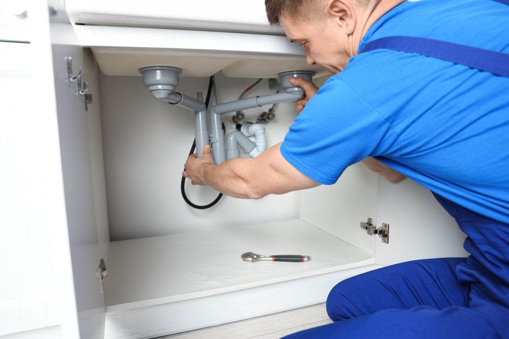 Why Professional Plumbing in Calgary Is Essential for Your Home? Plumber fixing pipes under sink indoors, closeup.