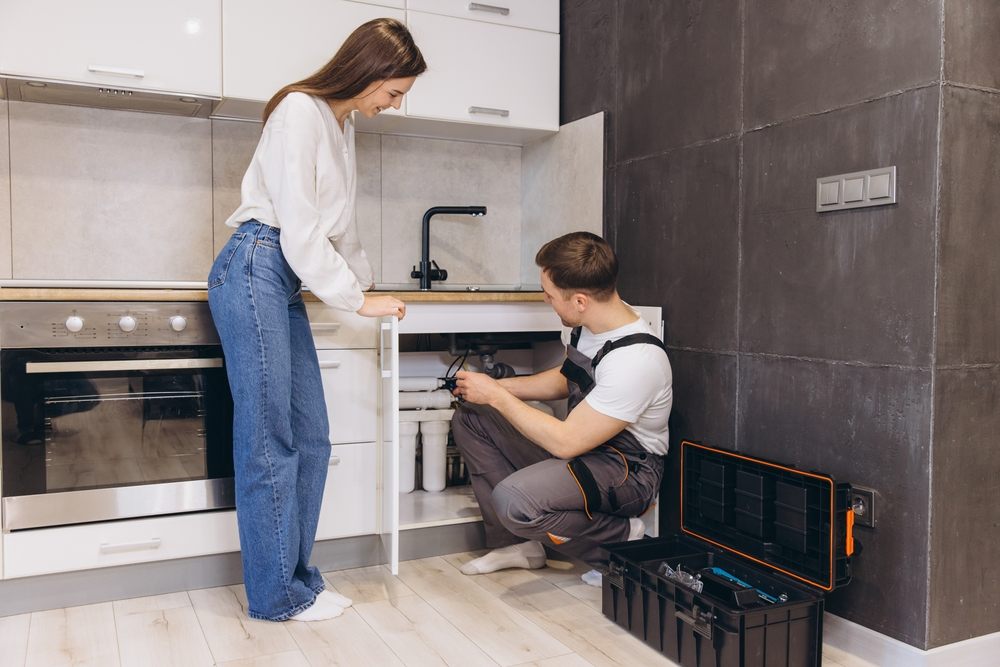 How to Choose the Right Plumbing Service in Calgary? Professional plumber working on sink pipes, installing water filter system in modern kitchen, while homeowner observes the process.