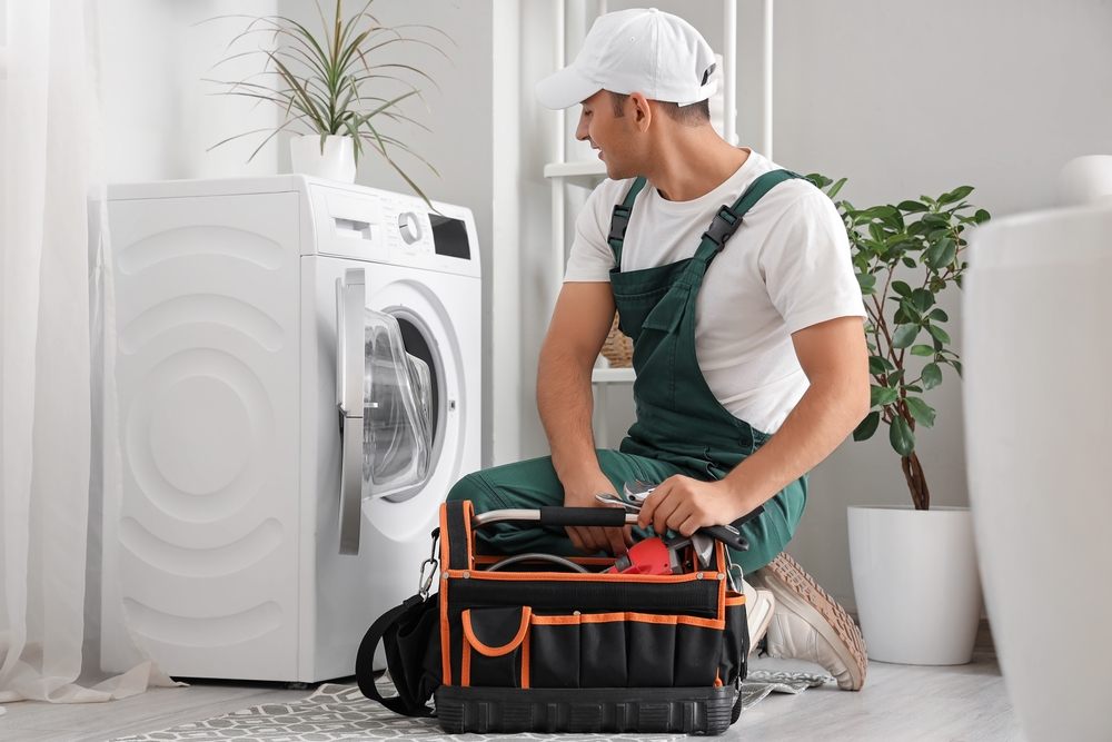How to Choose the Right Plumbing Service in Calgary? Male plumber with bag of tools fixing washing machine in bathroom.